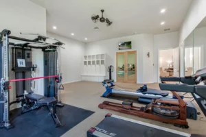 State-of-the-art home gym in Waxahachie luxury estate with premium exercise equipment, full mirrored walls, modern finishes, natural light, and adjacent sauna for health-focused living and daily wellness.