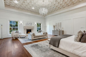 Serene primary suite in Waxahachie dream home featuring European-style coffered ceiling, elegant fireplace, crystal chandelier, hardwood floors, and luxurious finishes for a sophisticated master retreat.