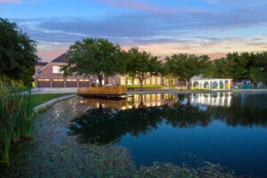 Picturesque evening reflection of Waxahachie luxury estate by private pond with elegant exterior lighting, waterfront views, and resort-style landscaping for tranquil Texas living.