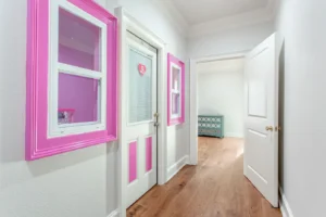 Creative kids' playroom in Waxahachie family home with pastel pink walls, organized bookshelves, educational toys, study desk, Barbie play area, and large windows for a fun and inspiring environment.