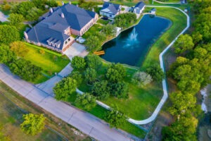 Stunning aerial view of private 5-acre Waxahachie estate showcasing expansive luxury home, manicured grounds, private pond with fountain, lush landscaping, and resort-style outdoor living spaces.